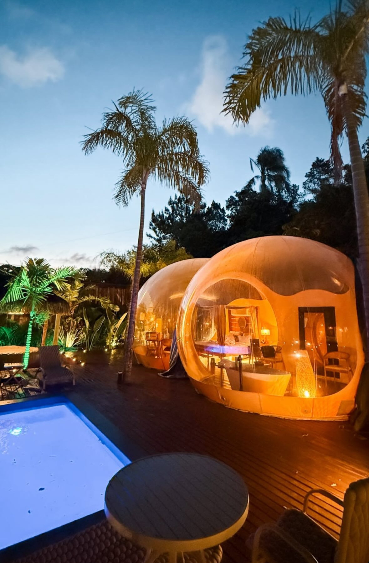 Bolhas de glamping iluminadas ao entardecer ao lado da piscina
