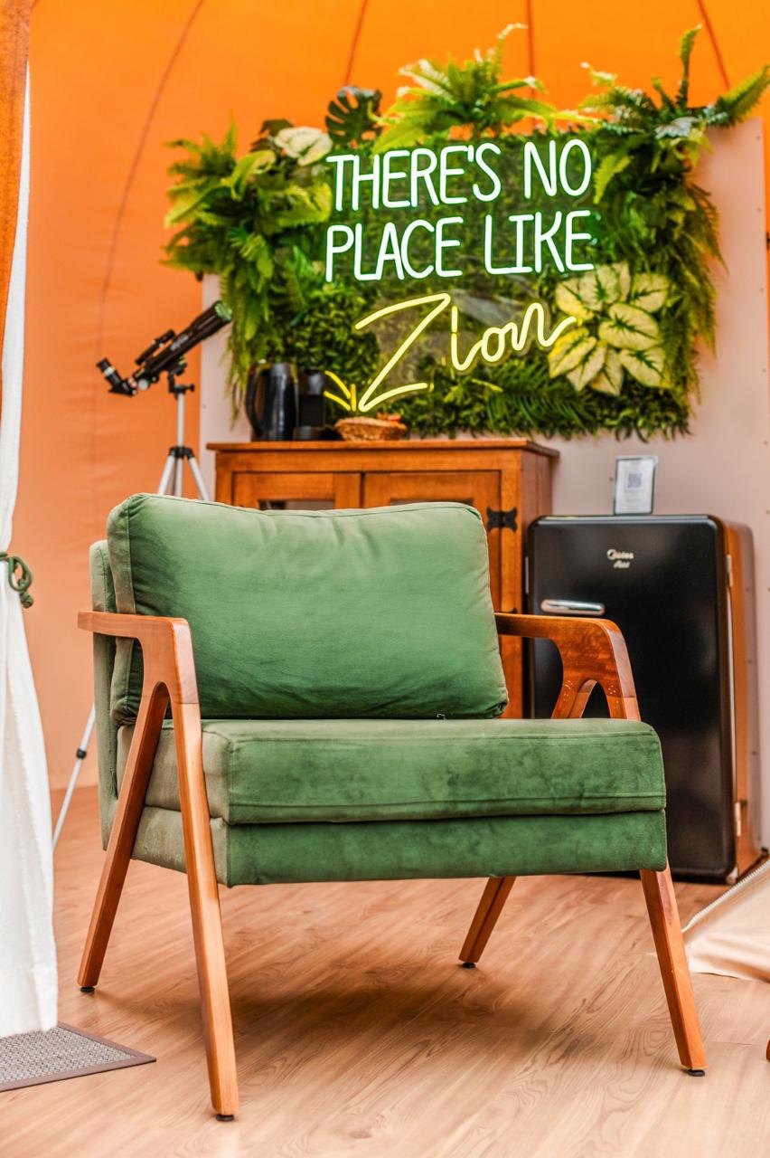 Interior de estar da unidade Zion, com poltrona verde e letreiro em neon There is no place like Zion